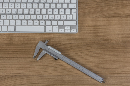 Modern keyboard and a sliding caliper on a wooden Desktopの写真素材