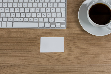 Modern keyboard a business card and a cup of coffee on a wooden Desktopの写真素材
