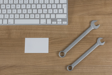 Modern keyboard two wrenches and a business card on a wooden Desktopの写真素材