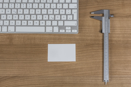 Modern keyboard a sliding caliper and a business card on a wooden Desktopの写真素材