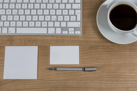 Modern keyboard a memo a business card a pen and a cup of coffee on a wooden Desktopの写真素材