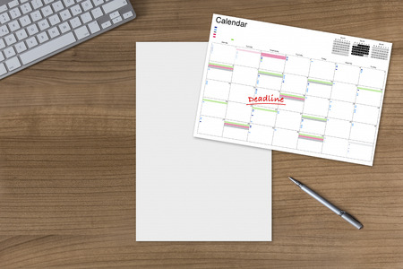 Calendar with the word Deadline and a blank sheet on a wooden table with modern keyboard and silver penの写真素材