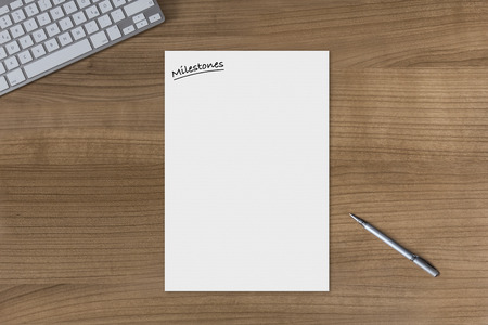 Blank sheet with the headline Milestones on a wooden table with modern keyboard and silver penの写真素材