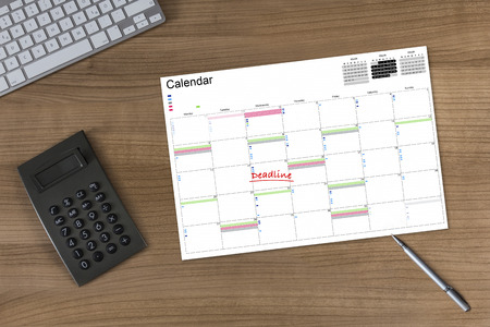 Calendar with the word Deadline on a wooden table with calculator modern keyboard and silver penの写真素材