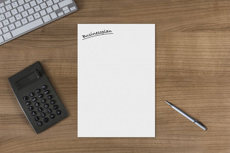 Blank sheet with the headline Businessplan on a wooden table with modern keyboard calculator and silver penの写真素材