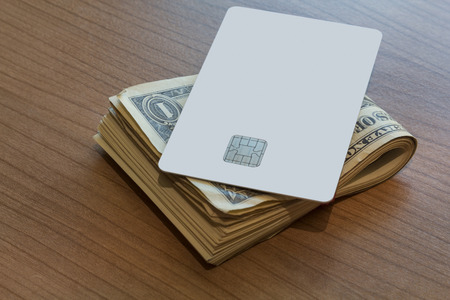 A Blank white Credit or Debit Card and a couple of dollar notes on a wooden tableの写真素材