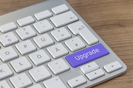 Upgrade written on a large blue button of a modern keyboard on a wooden desktopの写真素材