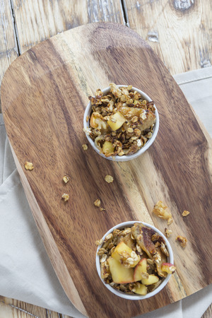 Two bowls of Apple Crumble on a wooden board on a rustic Tableの写真素材