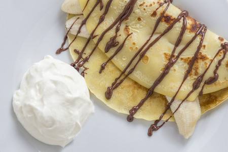 crepe filled with banana and chocolate sauce topping on a rustic wooden plateの写真素材