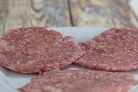 Three homemade hamburger patties on a plate on a rustic wooden tableの写真素材