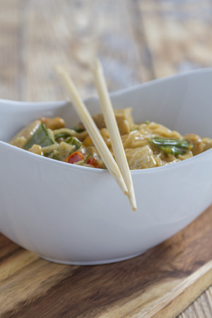 Bowl with traditional asian noodles vegetables and chicken on a rustic wooden table with chopsticksの写真素材