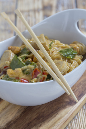 Bowl with traditional asian noodles vegetables and chicken on a rustic wooden table with chopsticksの写真素材