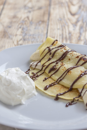 crepe filled with banana and chocolate sauce topping on a rustic wooden plateの写真素材