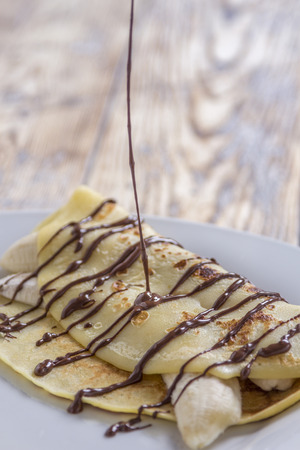 chocolate sauce pouring on crepe filled with banana on a rustic wooden plateの写真素材