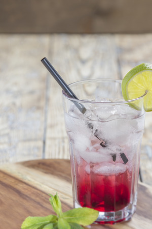 Glass with Red Drink on ice with lime slice and mint leaves on rustic wooden backgroundの写真素材
