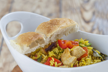 Bowl with curry flavored rice chicken and vegetables on rustic wooden tableの写真素材