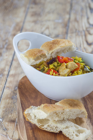 Bowl with curry flavored rice chicken and vegetables on rustic wooden tableの写真素材