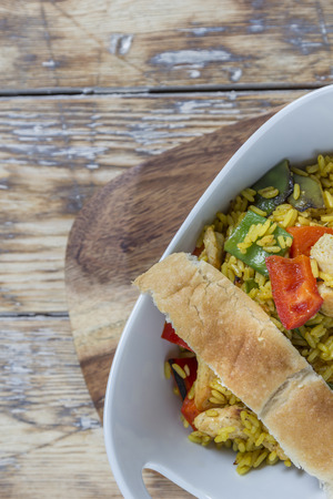 Bowl with curry flavored rice chicken and vegetables on rustic wooden tableの写真素材