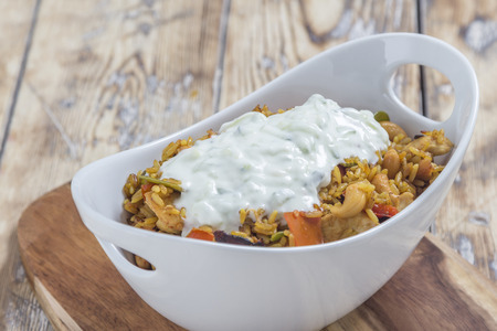 Bowl with curry flavored rice chicken and vegetables with garlic yoghurt sauce on rustic wooden tableの写真素材