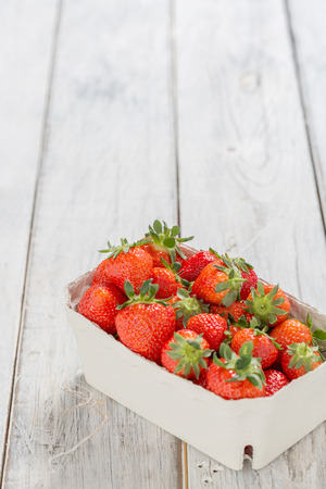 Strawberries in a paper bowl on a wooden tableの写真素材