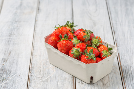 Strawberries in a paper bowl on a wooden tableの写真素材