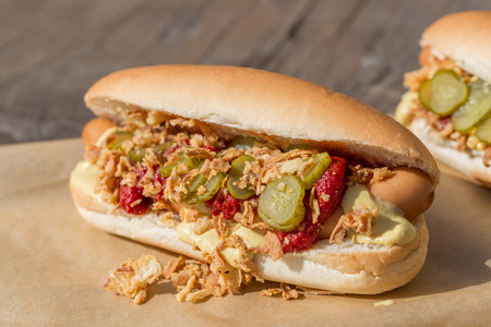 Hot Dog sausage in a bun with roasted onions, pickles, ketchup and mustard on rustic wooden backgroundの写真素材