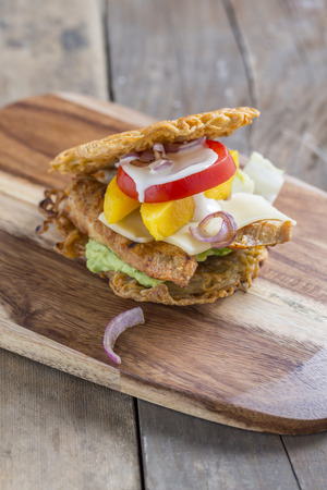 Burger made of asian Ramen noodles with chicken mango tomato cheese red onions and avocado creme on a rustic wooden tableの写真素材