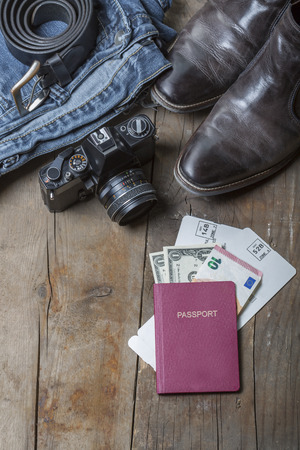 Jeans, Belt, leather boots, vintage camera and passport with tickets and money on a rustic wooden backgroundの写真素材