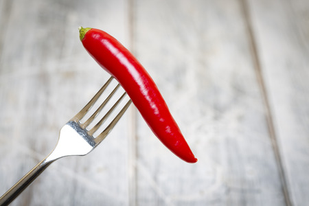 Red Chilli on fork over a rustic white blurred backgroundの写真素材