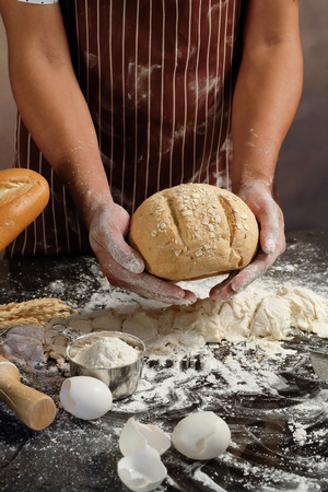Man preparing buns at table in bakery, Man sprinkling flour over fresh dough on kitchen table.