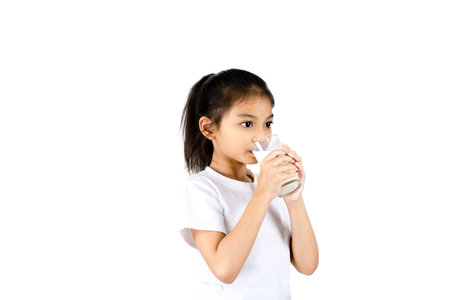 Young Asian girl in white t-shirt drinking milk from a glass isolated on white background with clipping path.の写真素材