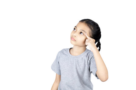 Asian little girl use finger pointing to her head looking at product or empty copy space while standing over isolated on white background with clipping path.の写真素材