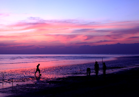 Silhouettes of people playing football on the beach when the sun sets in Thailandの写真素材