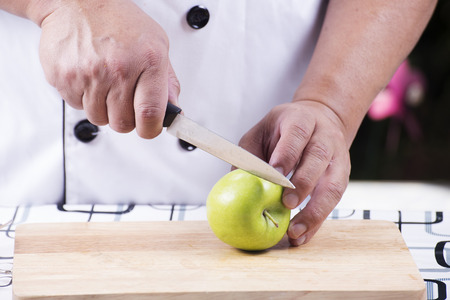 Chef's hands cutting green apple on wooden broadの写真素材