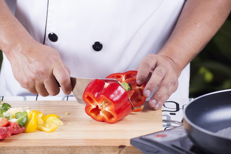 Chef cutting red bell pepper on wooden broadの写真素材