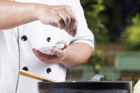 Chef putting Salt to the pan for cooking vegetableの写真素材
