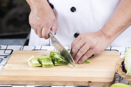 Chef cutting green lettuce on wooden broadの写真素材