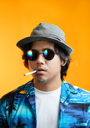 Hawaiian Gangster Smoking a Cigarette Wearing Fedora Hat and Sunglasses against Yellow Backgroundの写真素材