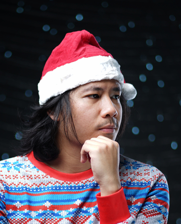 Thoughtful Asian Man Wearing Santa Hat and Christmas Sweaterの写真素材