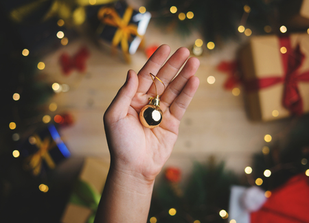 Hand Holding Small Gold Bauble Above Christmas Decoration. Top Viewの写真素材