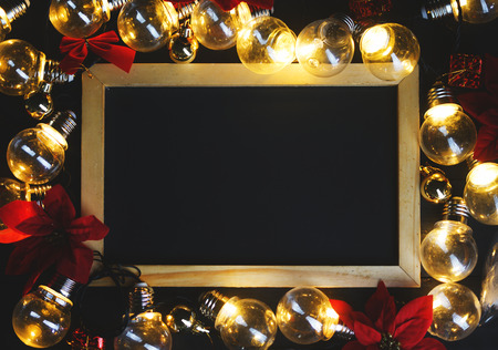 Blackboard Between Light Bulbs and Red Poinsettia on Black Wood. Top View Copy Space