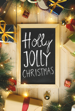 Top View of Holly Jolly Christmas Typography on Blackboard Surrounded By Christmas Gifts Ornamentの写真素材