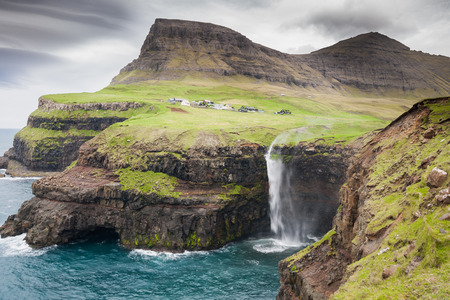 waterfall with the village Gasadalur in background on faroe islandsの写真素材