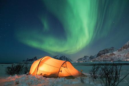 Illuminated tent under northern lights on Lofoten islands in winter