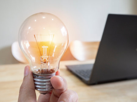 Women hand holding light bulb with laptop on wooden desk. The symbol of the idea, concept of new ideas with innovation and creativity.の写真素材