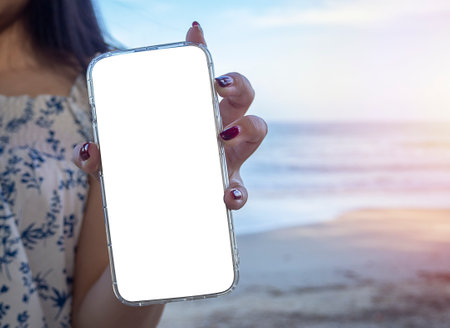 Hand of girl show using mobile phone with blank screen for mockup design on sea background. Modern social network information mobility concept.の写真素材