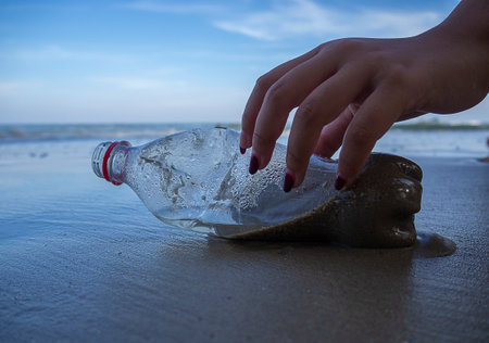 Volunteer or traveller collecting plastic bottle waste on the beach sand. Keep beach clean....