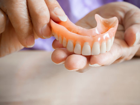 An elderly woman holds a denture. A woman is holding dentures in her hands. Removable dentures...