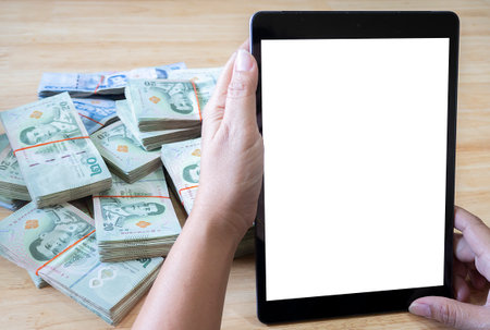 Close up of woman hands with white screen smartphone, tablet and stack of Thai banknotes. business, finance, saving, technology and people conceptの写真素材