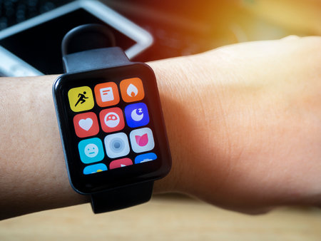Close up of the arm of Asian girl wearing a digital wrist watch and a blurred image of a mobile phone put on a notebook behide.の写真素材